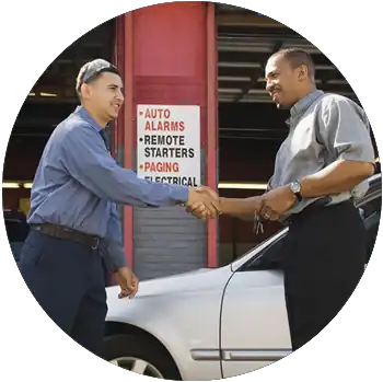 A young man working at an auto repair shop shakes a customer’s hand.
